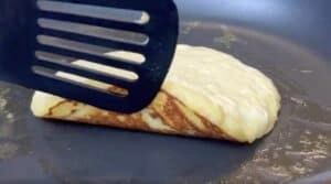 Flipping a golden brown pancake on a skillet with a spatula.